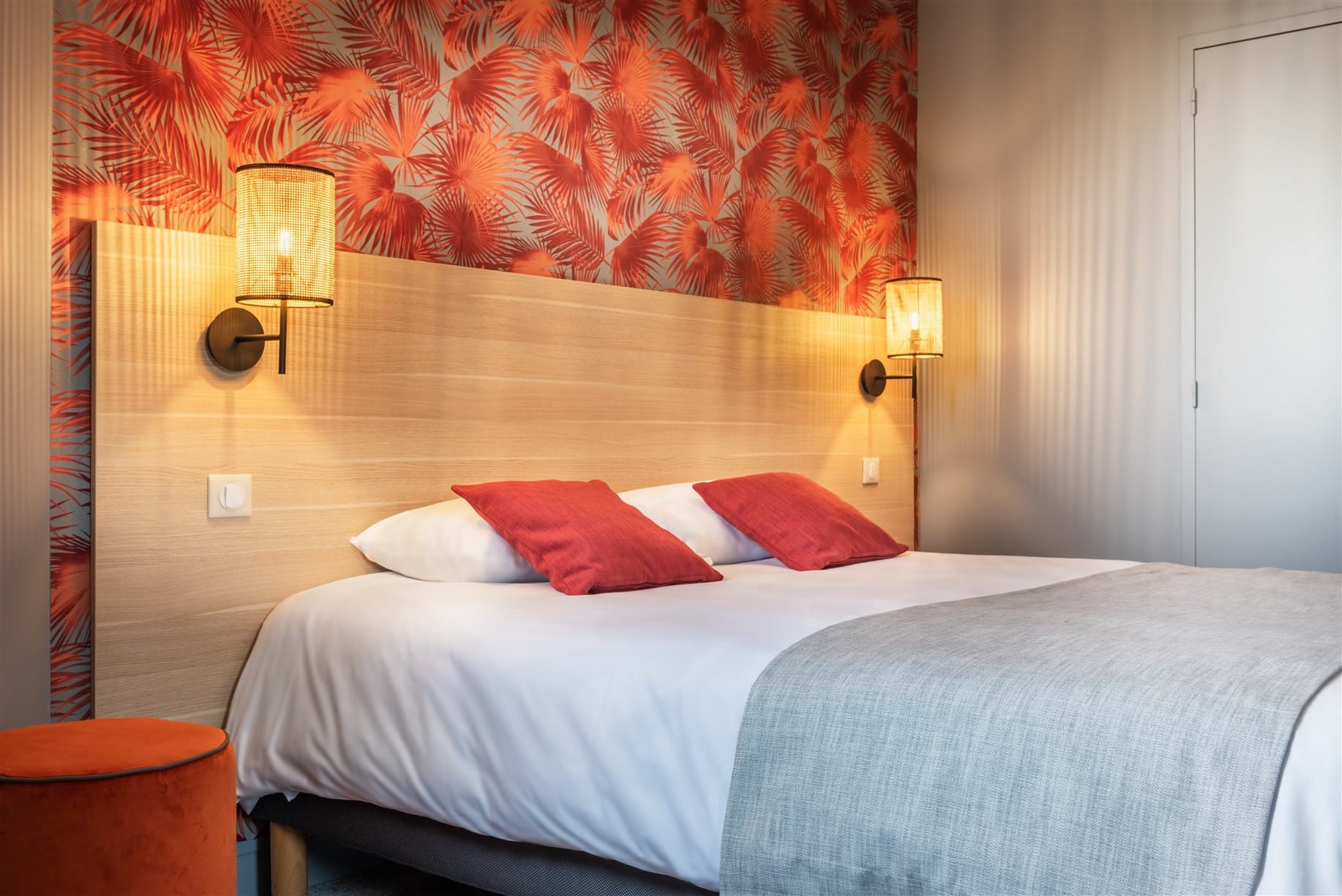 Vue ensemble tête de lit en chêne naturel et papier-peint feuillage rouge orange, coussin rouge applique rotin et pouf velours orange, par Virginie Vaudenay, décoratrice UFDI, à Sancerre dans le Cher(18), la Nièvre(58), le Loiret(45), l'Yonne(89), et Sologne(41)