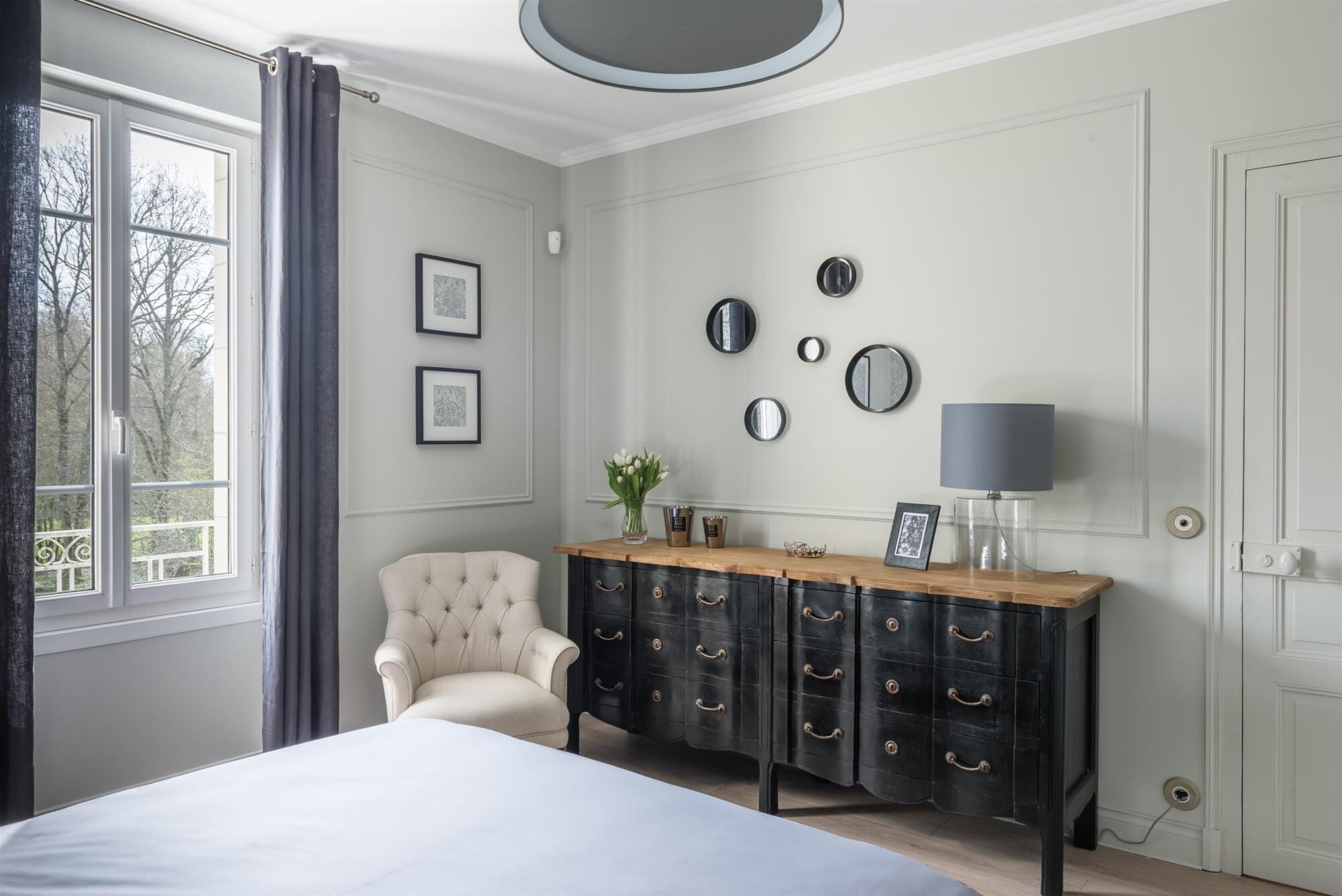 Vue commode ancienne noir et fauteuil capitonné beige, ensemble de miroirs ronds et rideaux en lin gris, par Virginie Vaudenay, décoratrice UFDI, à Sancerre dans le Cher(18), la Nièvre(58), le Loiret(45), l'Yonne(89), et Sologne(41)