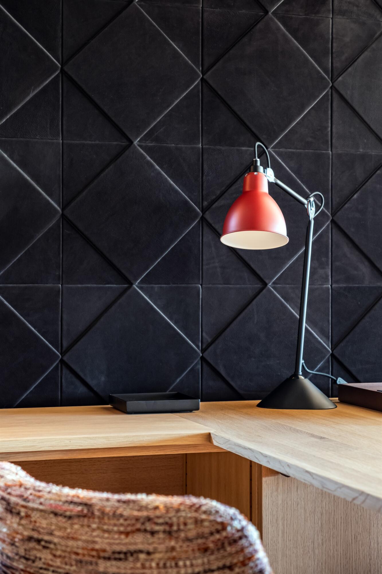 Gros plan mur dalles en cuir noir et lampe de bureau acier noir et rouge, par Virginie Vaudenay, décoratrice UFDI, à Sancerre dans le Cher(18), la Nièvre(58), le Loiret(45), l'Yonne(89), et Sologne(41)