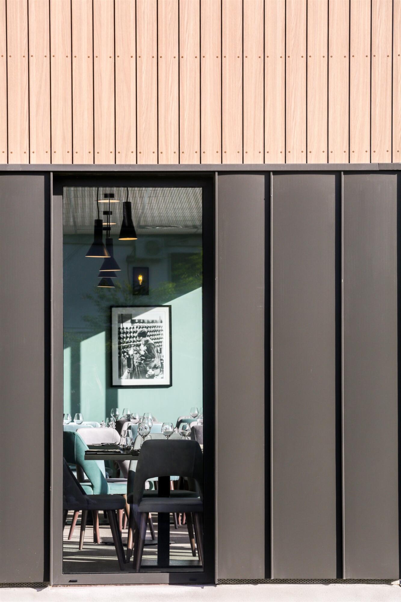Vue salle restaurant avec cadre affiche noir et blanc sur fond mur bleu glacé et suspensions acier noir, par Virginie Vaudenay, Décoratrice UFDI à Sancerre, dans le Cher (18), la Nièvre (58) , le Loiret (45) et L’Yonne (89), Sologne(41)